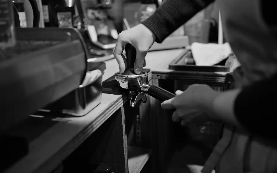 Barista tamping a portafilter in a dark cafe before open