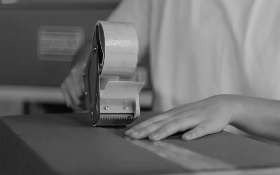 Hands taping a courier parcel on a packing bench
