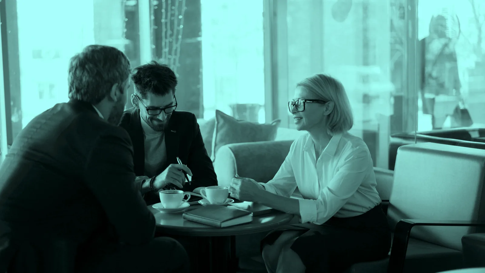 Two people talking over coffee at a table by a window, tinted teal