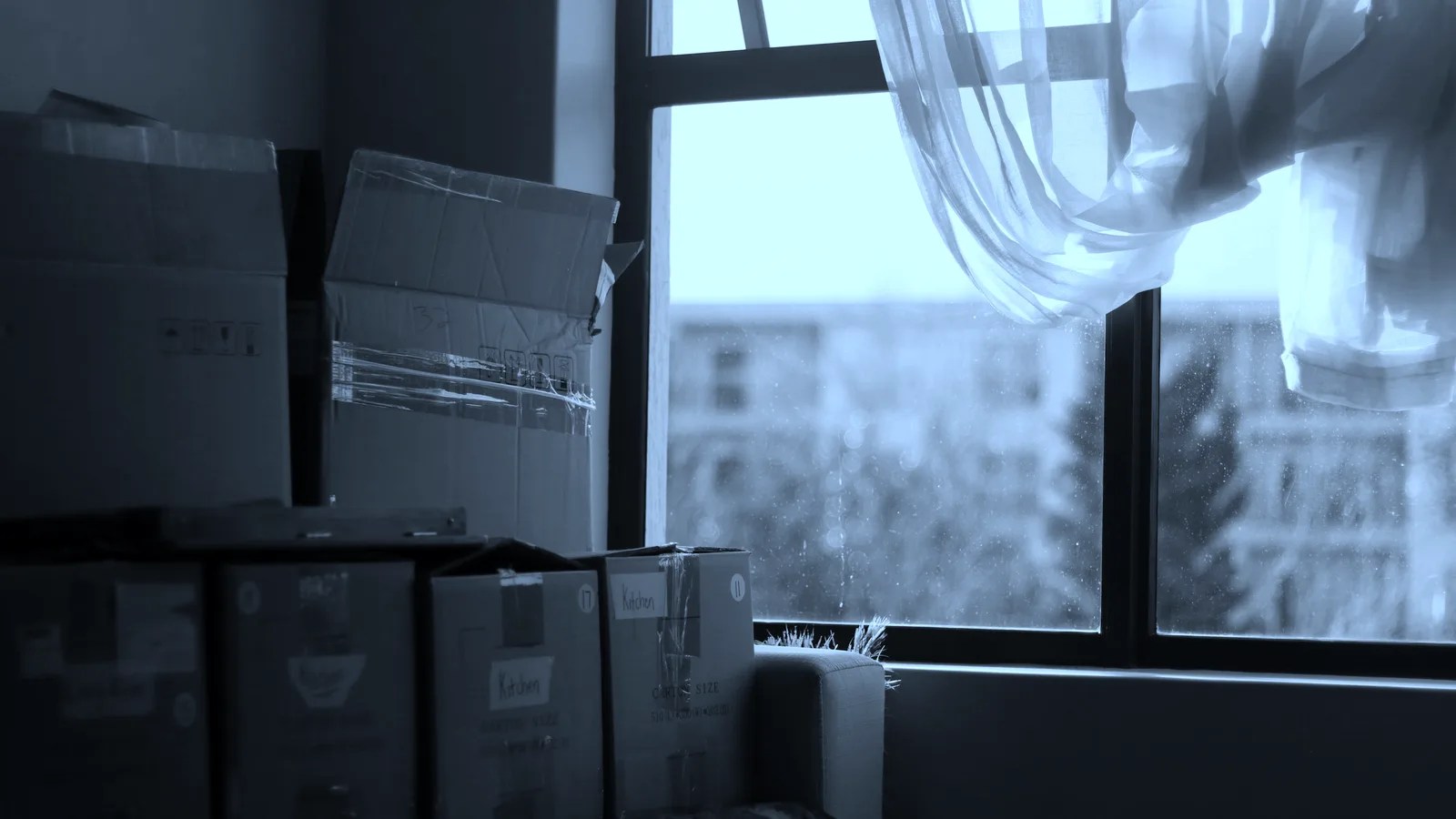 Packed boxes stacked in an empty room by a window, tinted blue
