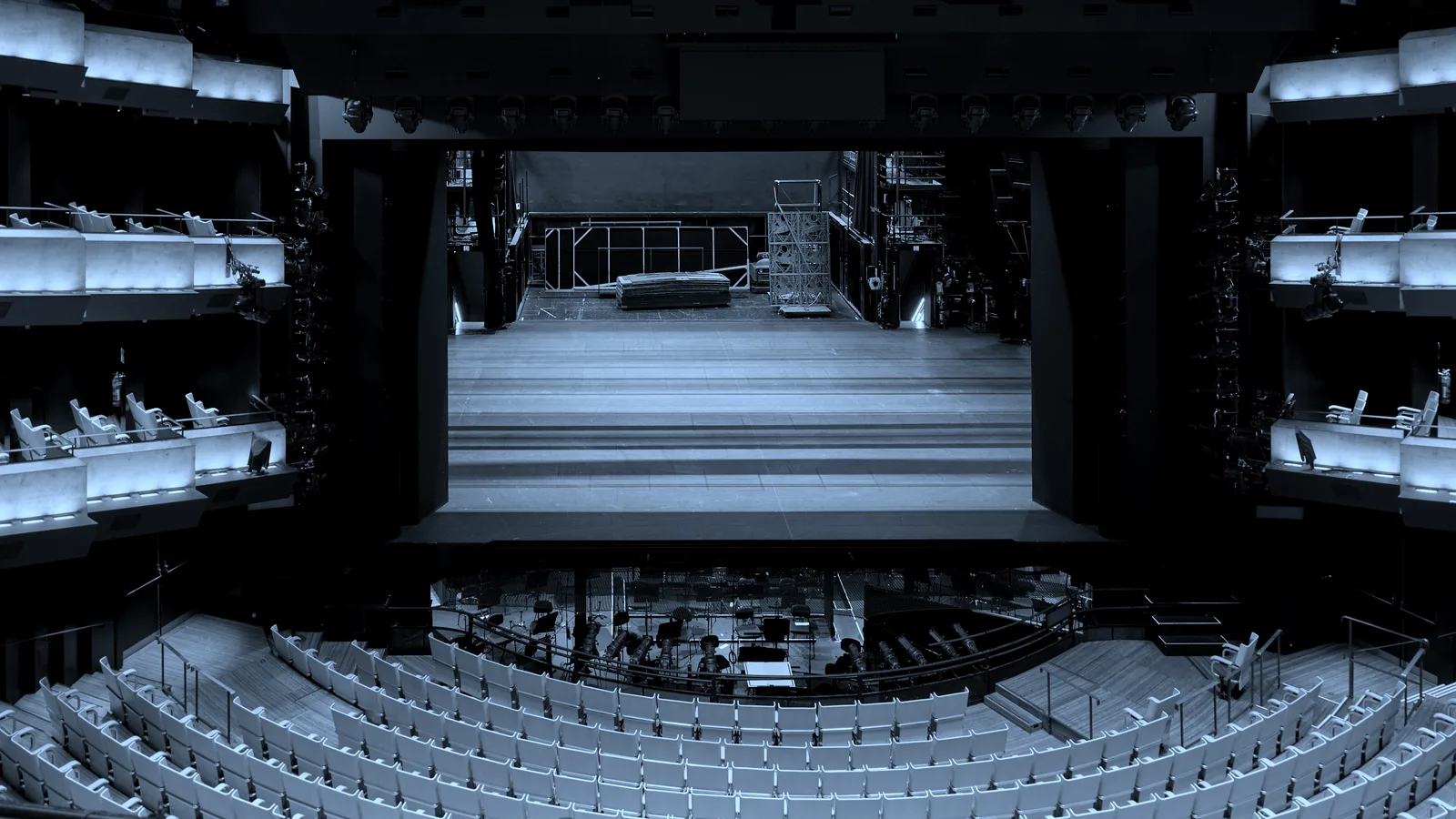 Rows of empty seats facing a lit stage, tinted blue