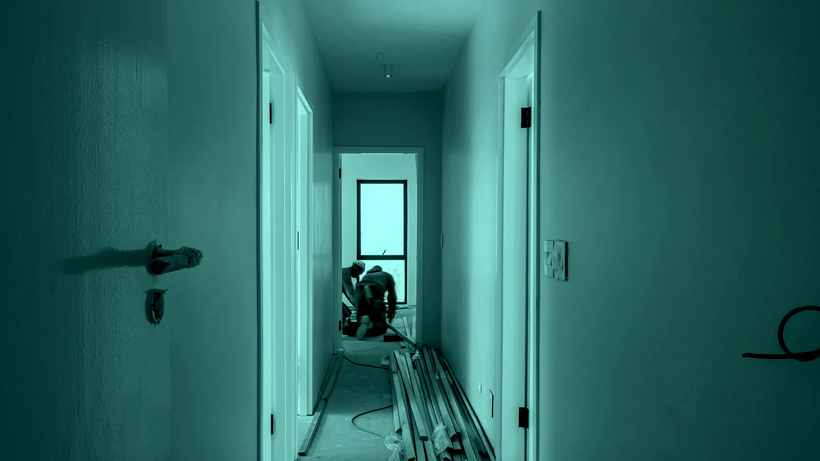 A freshly renovated hallway with a tradesperson working at the end, tinted teal