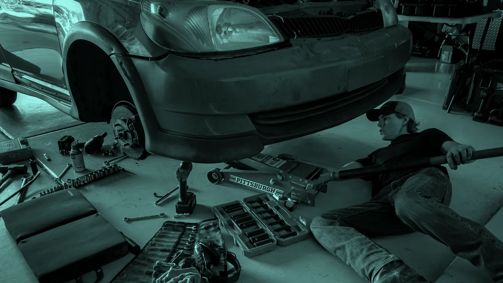 A mechanic working under a car on a jack, tinted teal