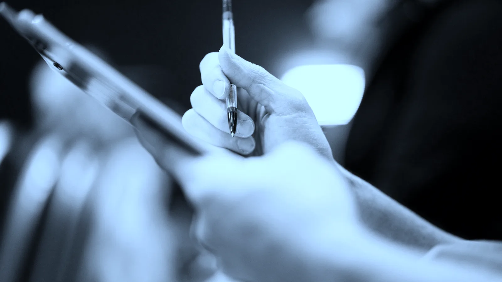 A hand working down a checklist on a clipboard, tinted blue