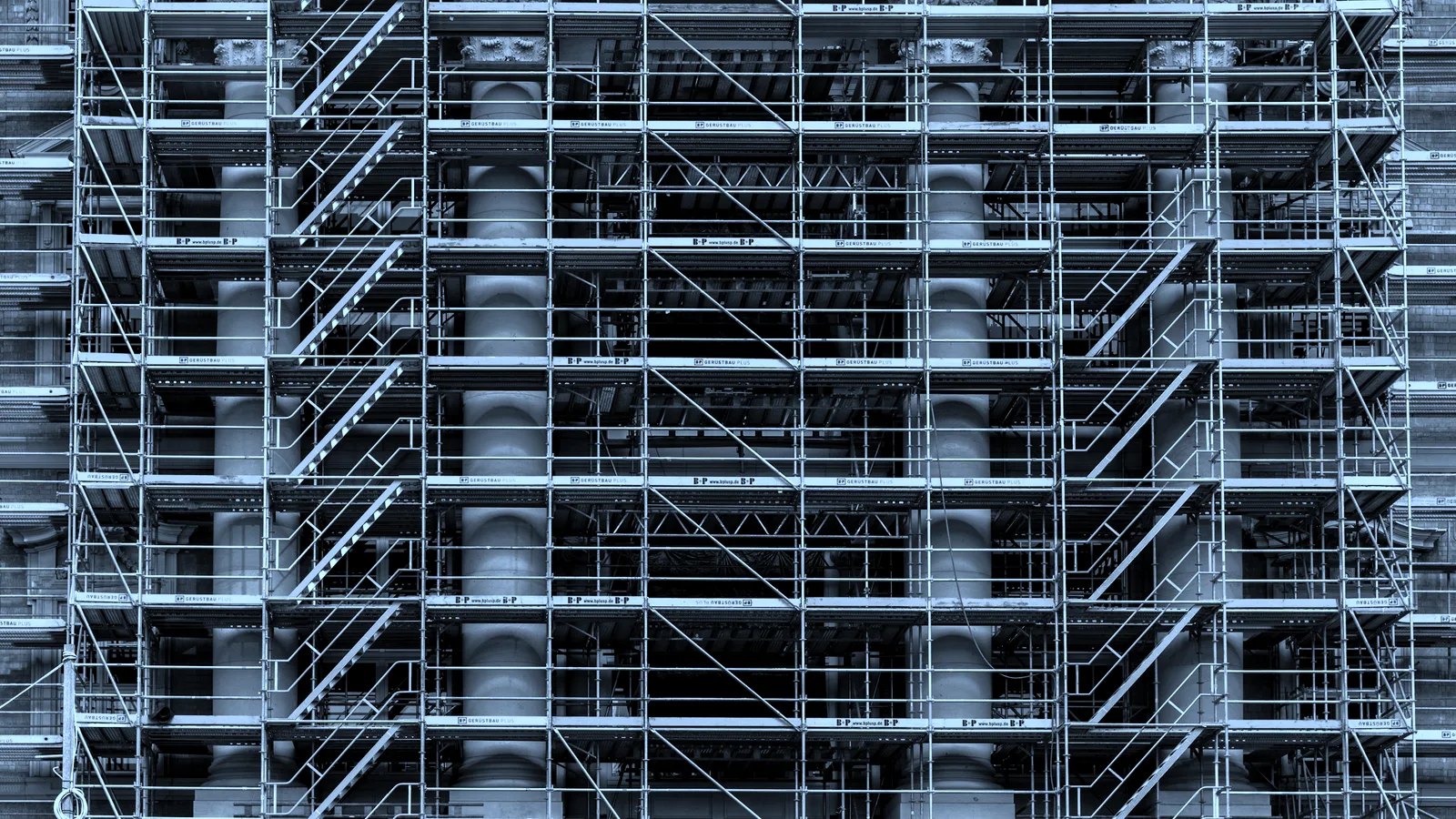 Scaffolding wrapped around an unfinished concrete building, tinted blue